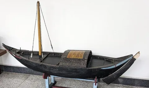 A traditional wooden boat with a mast, on display in a museum.